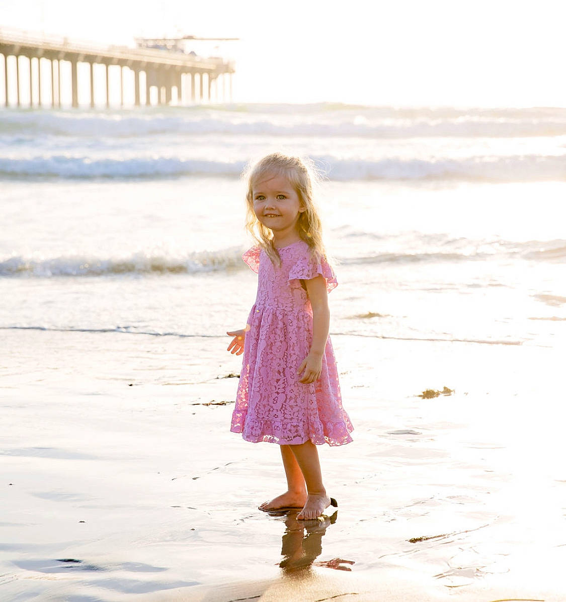 Lyla is registered to the contest to win money with this photo: beach, body_of_water, coastal_and_oceanic_landforms, dress, fun, hair, happy, horizon, joy, morning, natural_environment, one_piece_garment, people_in_nature, people_on_beach, person, shore, sky, standing, toddler, waist
