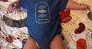 William is registered to the contest to win money with this photo: baby, infant, onesie, patterned_quilt, blue_clothing, face, arms, legs, lying_down, smiling, cute, child, indoor, fabric, colorful, playful, skin, head, expression, person