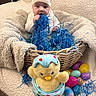 William joined the competition — help win amazing prizes! baby, child, basket, blanket, blue_shredded_paper, plush_toy, stuffed_animal, easter_eggs, colorful, hat, cozy, indoors, cute, soft_texture, playful, seated, toy, holiday, decor, infant