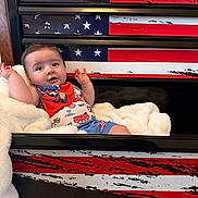 William joined the competition — help win amazing prizes! baby, infant, blanket, drawer, american_flag, red, blue, white, clothing, bib, cartoon, car, pattern, face, arms, smiling, indoor, furniture, cozy, child