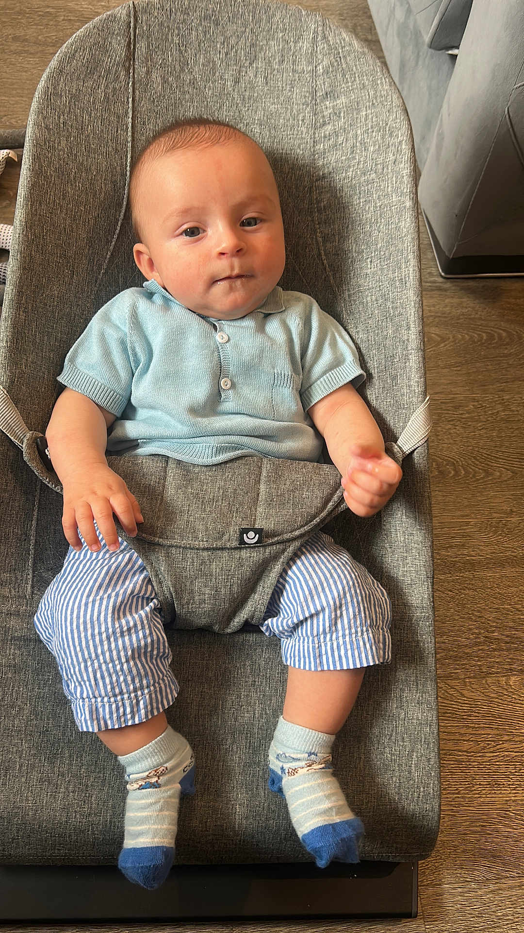 Aron is registered to the contest to win money with this photo: baby, infant, child, baby_seat, blue_shirt, striped_pants, socks, wooden_floor, gray_fabric, indoor, cute, portrait, young_child, seated, comfortable, curious, person, casual_clothing, home_interior, relaxed