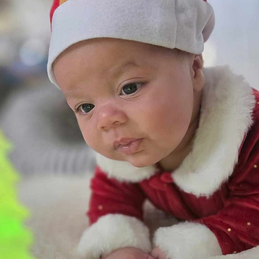Iam Ricardo joined the competition — help win amazing prizes! baby, child, christmas, closeup, curious, cute, festive, holiday, holiday_decoration, indoors, infant, lying_down, ornament, portrait, red_clothing, reindeer_hat, santa_hat, soft_texture, warm_lighting, white_fur