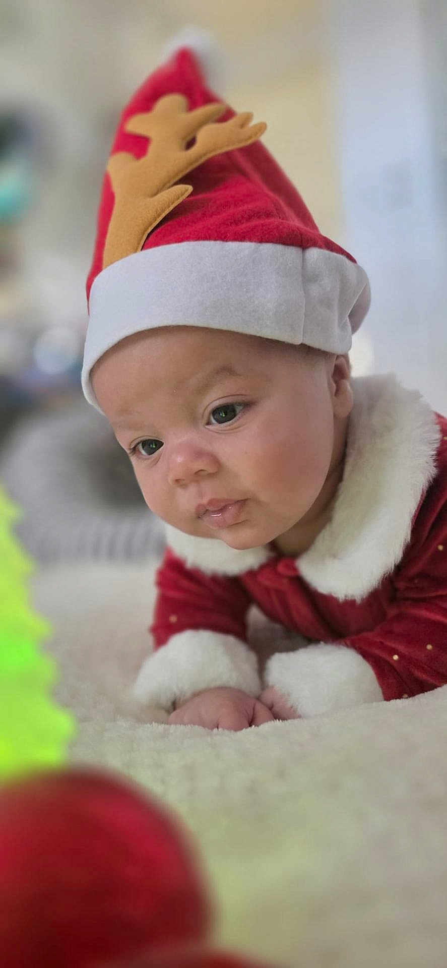 Iam Ricardo joined the competition — help win amazing prizes! baby, infant, child, christmas, holiday, santa_hat, reindeer_hat, red_clothing, white_fur, soft_texture, curious, indoors, closeup, portrait, festive, holiday_decoration, ornament, lying_down, cute, warm_lighting
