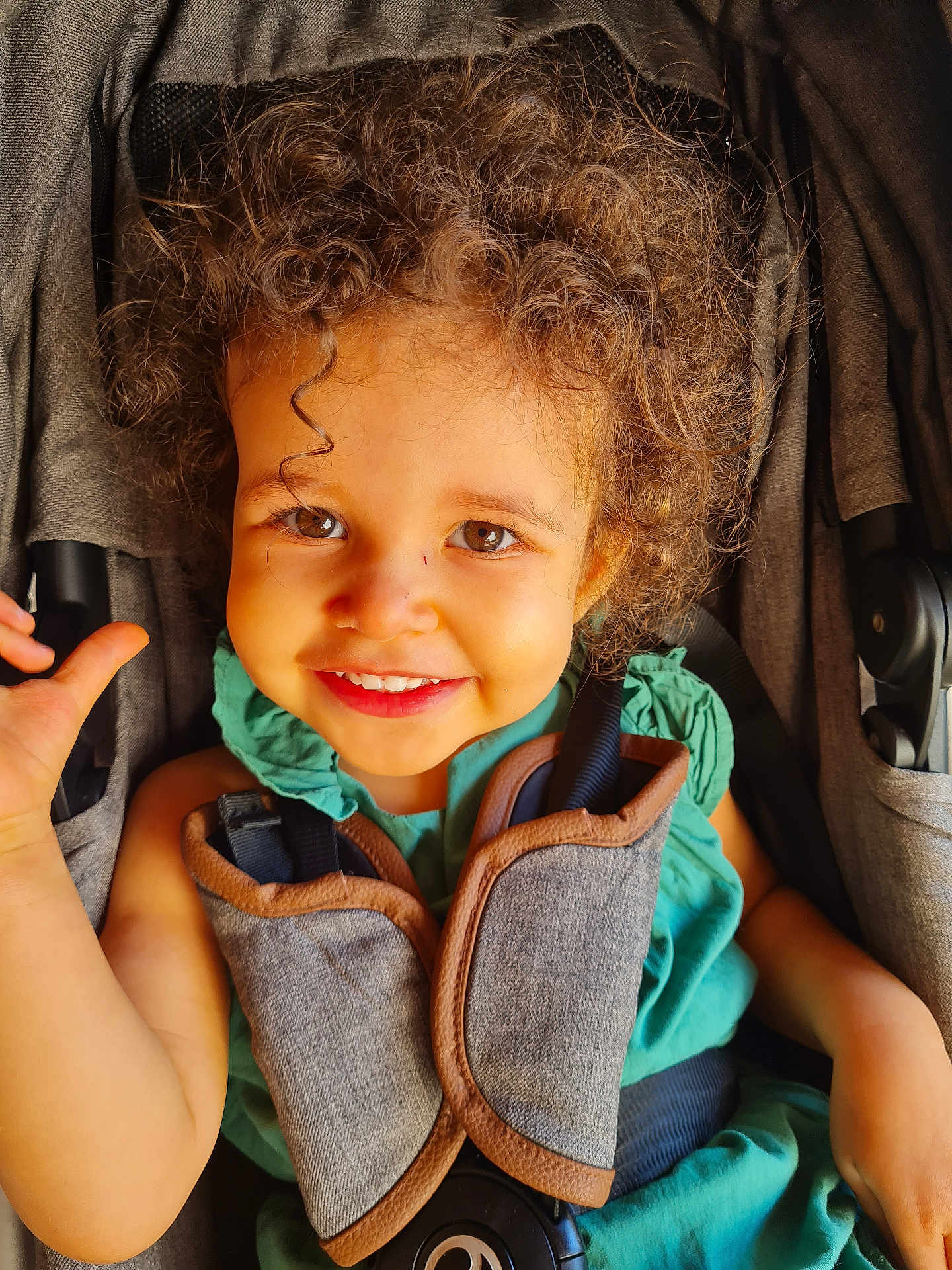 Laïna a rejoint le concours — aidez-le/la à gagner de superbes lots ! baby, baby_carrier, brown_eyes, child, childhood, closeup, curly_hair, cute, daylight, green_clothing, happy, infant, outdoor, person, portrait, seat, seatbelt, smiling, stroller, toddler