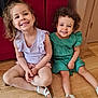 casual_clothing, child, children, curly_hair, cute, floor, green_dress, happy, home, indoors, person, portrait, purple_top, red_couch, sitting, smiling, two_people, white_sandals, wooden_floor, young