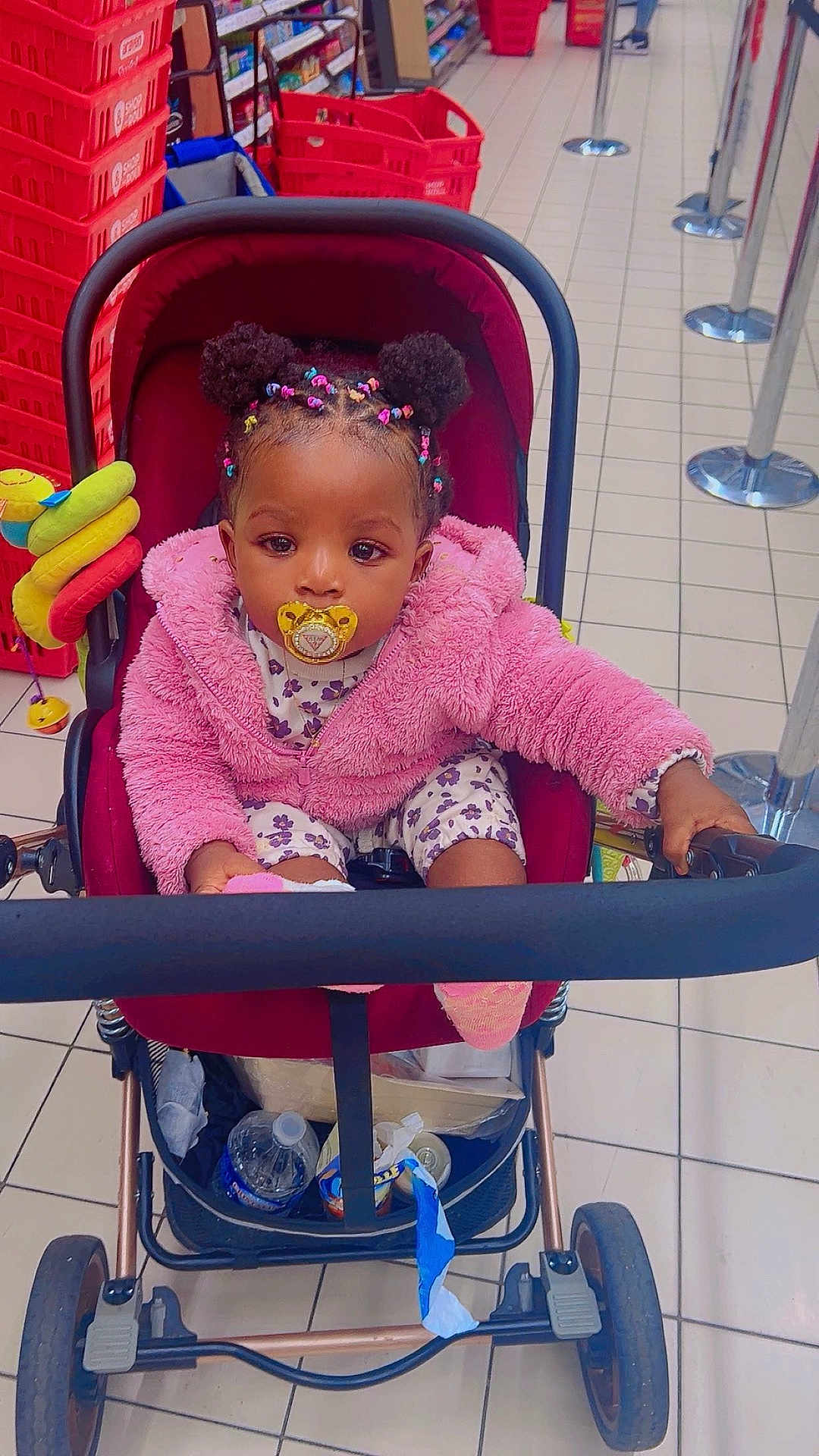 Saskia a rejoint le concours — aidez-le/la à gagner de superbes lots ! toddler, child, stroller, pacifier, pink_jacket, colorful_hair, supermarket, shopping_basket, floor_tiles, baby, toy, water_bottle, clothing, indoor, person, shopping_cart, cute, seated, portrait, retail
