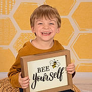 Elijah is registered to the contest to win money with this photo: blonde, bodypart, boy, child, clothing, face, finger, hand, happy, head, male, person, photoframe, photography, portrait, sitting, smile, t_shirt, text, wood
