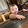 Miles is registered to the contest to win money with this photo: baby, child, table, wood, hand, face, curious, indoor, furniture, chair, eyes, expression, person, young, cute, brown_clothing, restaurant, interior, wooden_wall, lighting