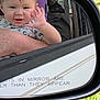 Miles is registered to the contest to win money with this photo: baby, child, car, side_mirror, reflection, waving, hand, face, window, seatbelt, car_seat, grass, outdoor, person, portrait, cute, smiling, arm, clothing, vehicle