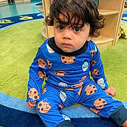 Zyon Levo is registered to the contest to win money with this photo: toddler, child, pajamas, blue, milk, cookie, sitting, rug, classroom, floor, curly_hair, indoor, playroom, furniture, expression, person, cute, young, clothing, colorful