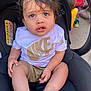 Zyon Levo joined the competition — help win amazing prizes! toddler, child, car_seat, nike_tshirt, shorts, barefoot, curly_hair, outdoor, pavement, person, young_child, casual_clothing, seated, black_car_seat, warning_label, sunlight, background_child, yellow_shirt, green_shoes, expression