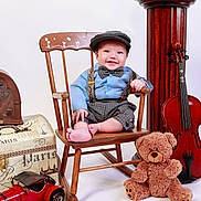 Josias is registered to the contest to win money with this photo: baby, child, vintage_clothing, bow_tie, suspenders, wooden_chair, teddy_bear, violin, toy_car, old_radio, smiling, indoor, portrait, cute, hat, props, classic_style, studio_photo, happy, person