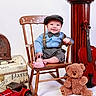 baby, child, vintage_clothing, bow_tie, suspenders, wooden_chair, teddy_bear, violin, toy_car, old_radio, smiling, indoor, portrait, cute, hat, props, classic_style, studio_photo, happy, person