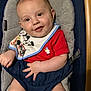 Levon is registered to the contest to win money with this photo: baby, baby_chair, bib, blue, child, cushion, face, grey, hand, happy, head, indoors, infant, legs, mickey_mouse, person, red_shirt, seated, skin, smiling