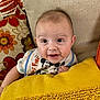 baby, blanket, child, clothing, comfort, couch, cute, eyes, face, flower_pattern, home, indoor, infant, orange, pillow, portrait, sitting, smile, textile, yellow