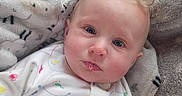 Emery is registered to the contest to win money with this photo: baby, child, infant, curly_hair, blue_eyes, onesie, animal_print, blanket, soft_texture, cozy, cute, portrait, indoors, face, expression, child_clothing, resting, comfort, young_child, closeup
