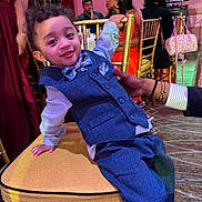 Lazhi Solomon is registered to the contest to win money with this photo: toddler, child, boy, suit, bow_tie, chair, party, indoor, smile, curly_hair, person, fashion, event, people, furniture, hand, background, dress, lighting, candid