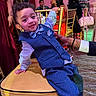 toddler, child, boy, suit, bow_tie, chair, party, indoor, smile, curly_hair, person, fashion, event, people, furniture, hand, background, dress, lighting, candid