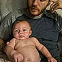 baby, adult, man, child, blanket, couch, indoor, portrait, relaxing, holding, clothing, facial_hair, tattoo, diaper, expression, seated, skin, person, home, comfort