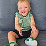 baby, child, smiling, sitting, couch, green_hoodie, black_shorts, sneakers, happy, blue_eyes, clapping, indoor, portrait, cute, infant, light_hair, casual_clothing, footwear, person, young