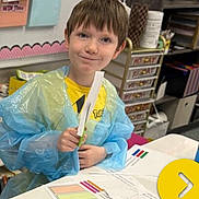 Hunter is registered to the contest to win money with this photo: child, classroom, portrait, smiling, art_project, paintbrush, blue_smocks, crafts, worksheets, pencils, markers, school, desk, colorful, indoor, learning, creative, supplies, young_person, photograph