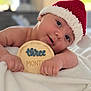 baby, infant, child, santa_hat, red_hat, white_blanket, soft_texture, wooden_sign, three_months, cute, portrait, indoor, close_up, smiling, holiday, christmas, festive, face, hands, lying_down