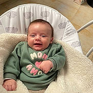 Essil a rejoint le concours — aidez-le/la à gagner de superbes lots ! baby, smiling, indoor, blanket, green_sweatshirt, cushion, face, infant, cozy, clothing, person, happy, head, seated, floor_tiles, baby_seat, warm_lighting, cute, child, home