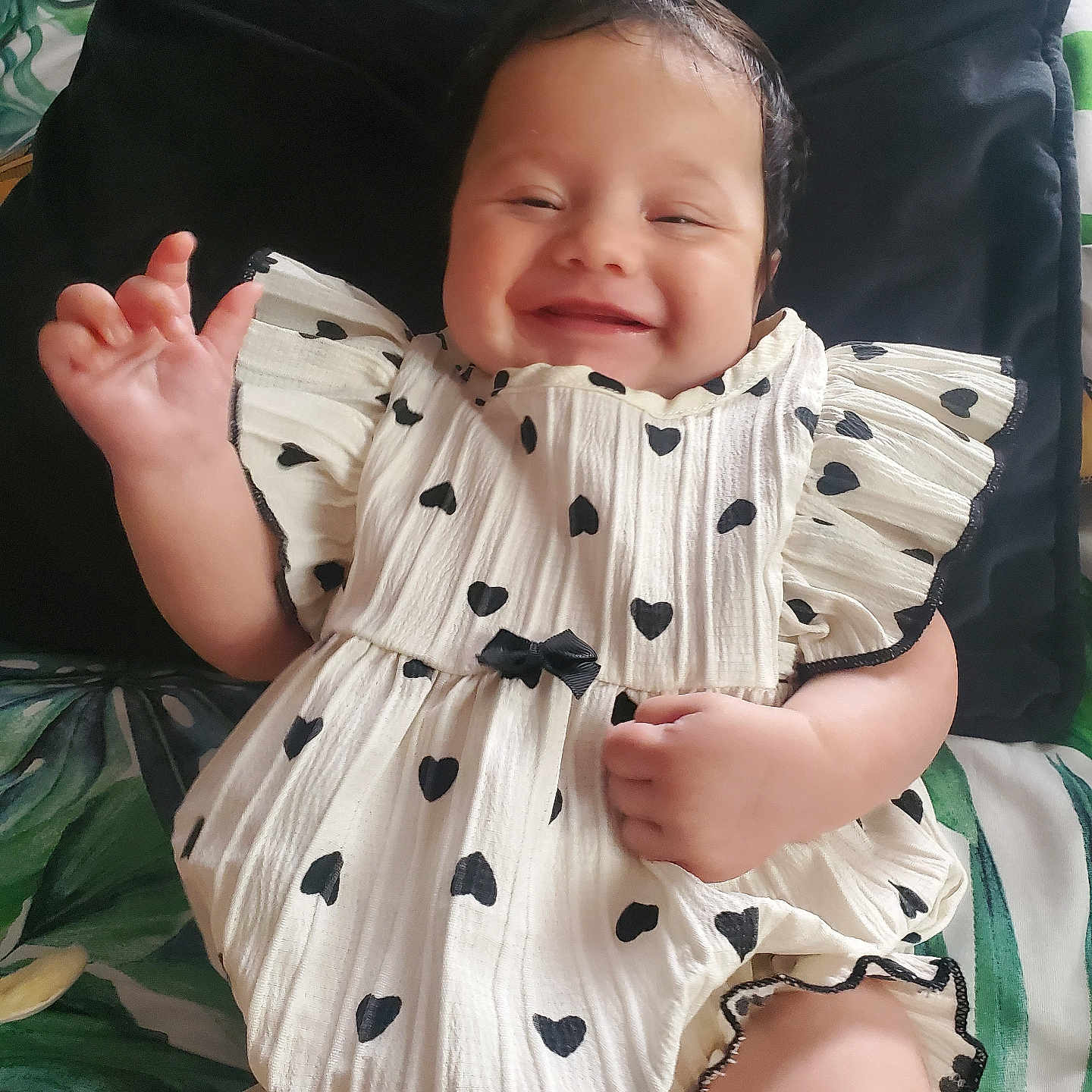 Nellie-Grace joined the competition — help win amazing prizes! baby, black_hearts, blanket, child, comfort, cushion, cute, dress, face, hand, happy, indoors, infant, lying_down, pattern, person, playful, portrait, smiling, white_dress