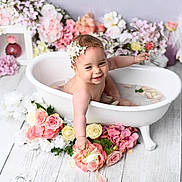 Lou a rejoint le concours — aidez-le/la à gagner de superbes lots ! baby, bathtub, water, flowers, flower_petals, headband, smiling, happy, infant, white_tub, pink_flowers, yellow_flowers, decor, wooden_floor, splashing, cute, portrait, indoor, child, flower_arrangement