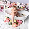 baby, bathtub, water, flowers, flower_petals, headband, smiling, happy, infant, white_tub, pink_flowers, yellow_flowers, decor, wooden_floor, splashing, cute, portrait, indoor, child, flower_arrangement
