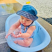 Micah is registered to the contest to win money with this photo: toddler, child, water, splashing, hat, blue_hat, romper, outdoor, sunny, tub, pavement, gravel, baby, playing, summer, cute, sitting, water_play, sunlight, fun