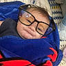 baby, blanket, blue_blanket, child, cozy, cushion, cute, eyewear, face, floor, glasses, home, indoors, patterned_rug, portrait, red_blanket, smiling, soft_toy, toddler, wrapped