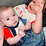 baby, child, couch, denim_overalls, hand, face, curious, playful, casual_clothing, indoor, person, infant, cute, relaxed, sitting, two_children, red_shirt, white_shirt, denim, soft_fabric