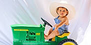 Lucas is registered to the contest to win money with this photo: toddler, child, toy_tractor, john_deere, cowboy_hat, overalls, blue_clothing, green_toy, yellow_wheels, barefoot, cute, portrait, studio_shot, white_backdrop, sitting, playtime, outdoor_toy, young_child, curious_expression, baby