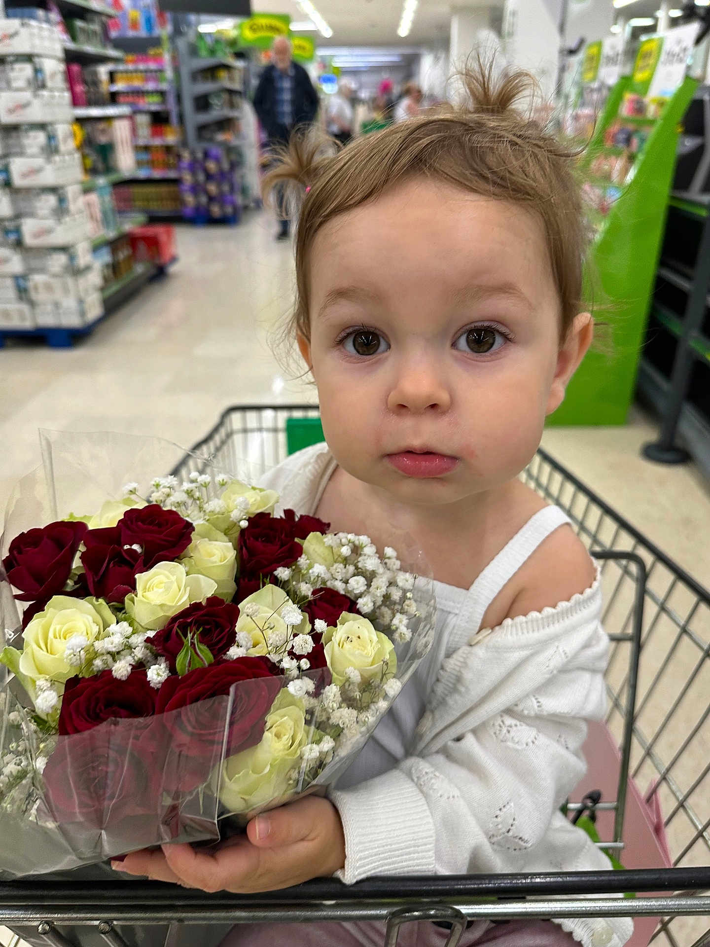 Mia joined the competition — help win amazing prizes! toddler, child, shopping_cart, flowers, roses, bouquet, supermarket, aisle, grocery_store, white_clothing, pigtails, curious, person, indoor, retail, baby, cute, holding, face, portrait
