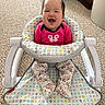 Keanna is registered to the contest to win money with this photo: baby, child, infant, smiling, sitting, baby_seat, patterned_clothing, pink_shirt, floral_pants, carpet, toys, indoor, happy, cute, person, face, home, play_area, comfort, joy