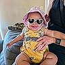 Durrann is registered to the contest to win money with this photo: adult, baby, child, comfort, couch, cute, face, floral_pattern, hand, happy, hat, indoor, person, sitting, skin, smile, sunglasses, sunhat, watch, yellow_clothing