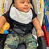 Davontae is registered to the contest to win money with this photo: baby, bib, black_shirt, camouflage_pants, car_seat, child, cute, face, hand, happy, infant, person, plush_toy, retail, seatbelt, shoe, shopping, shopping_cart, store_aisle, warning_label