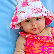 Elya participe au concours pour gagner de l'argent avec cette photo : baby, child, face, hat, bucket_hat, swimsuit, pink, orange, seashell_pattern, skin, blue_background, infant, cute, summer, outdoor, portrait, smile, baby_fashion, chubby_cheeks, relaxing