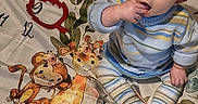 Nova joined the competition — help win amazing prizes! baby, child, milestone_blanket, striped_clothing, sitting, curious, hand_in_mouth, animal_illustrations, monkey, giraffe, elephant, plush, floor, indoor, cute, portrait, young_child, knitted_sweater, patterned_leggings, colorful