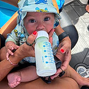 Buck joined the competition — help win amazing prizes! baby, bottle, feeding, hoodie, infant, person, hand, nail_polish, legs, feet, seat, sunlight, shadow, outdoor, clothing, skin, cute, expression, closeup, water