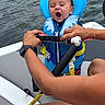 baby, life_jacket, water, boat, hands, person, yawning, sitting, outdoor, water_sports, summer, safety, child, life_safety, adult, water_surface, grip, nautical, daytime, recreation