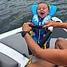 Buck is registered to the contest to win money with this photo: baby, life_jacket, water, boat, hands, smile, child, outdoor, person, safety, joy, summer, recreation, fun, blue, seat, rope, watch, clothing, nature