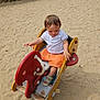 casual_clothing, child, daylight, elephant, fun, happy, outdoor, park, play, playground, recreation, rocking_toy, sand, sandals, shorts, smiling, summer, toddler, toy, wood