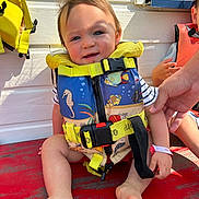 Maylonn participe au concours pour gagner de l'argent avec cette photo : baby, barefoot, blue, child, fish_pattern, hand, life_jacket, outdoor, person, playful, red_surface, safety, sitting, smiling, striped_shirt, sunlight, toddler, white_wall, window, yellow