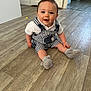 baby, child, cute, eyes, face, floor, footwear, hand, happy, home, indoor, infant, overalls, person, plush_slippers, sitting, smiling, striped_clothing, white_shirt, wooden_floor