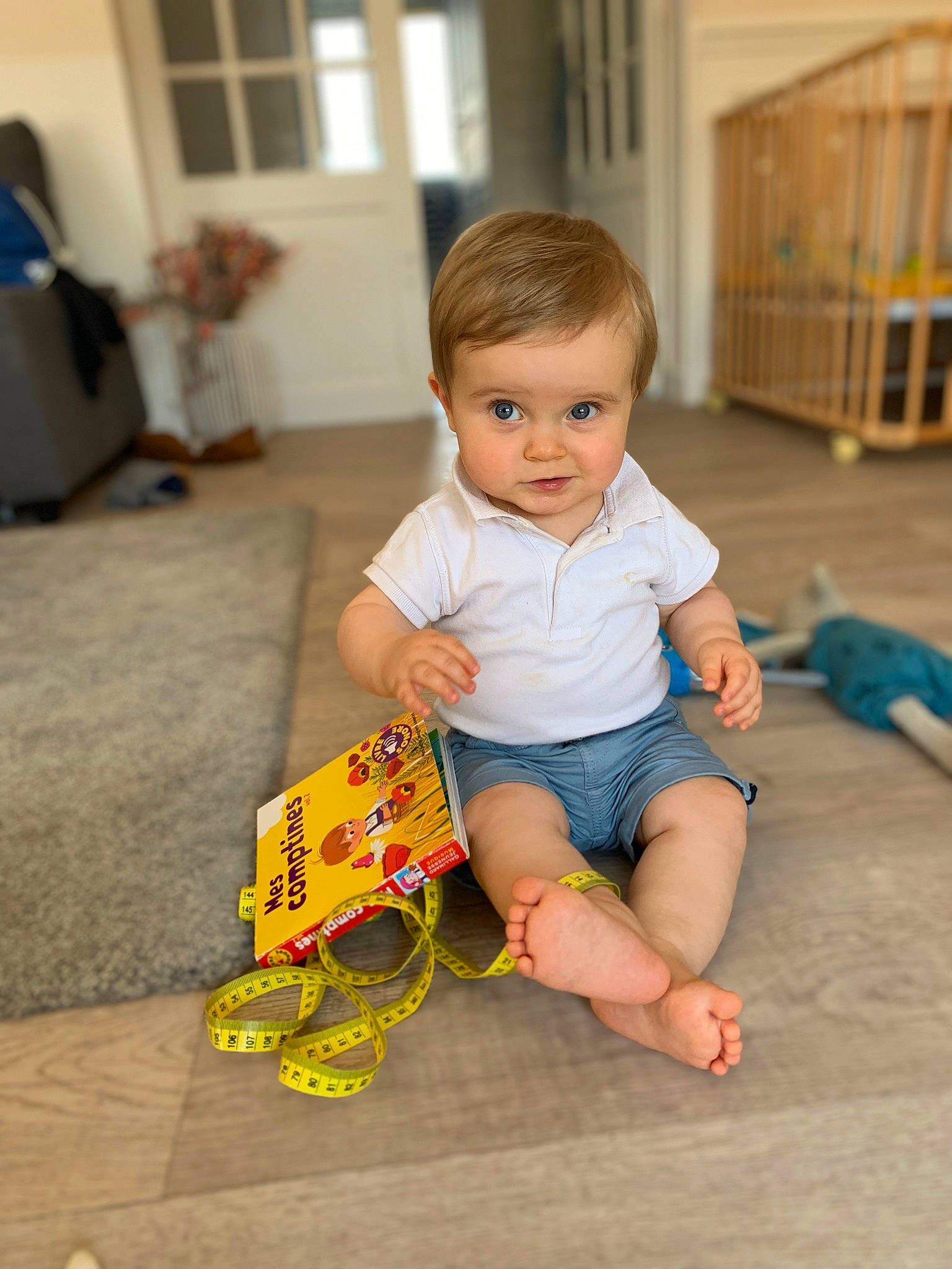Arsène participe au concours pour gagner de l'argent avec cette photo : baby_toddler_clothing, barefoot, child, facial_expression, floor, flooring, foot, fun, happy, hardwood, human_leg, knee, leisure, mammal, person, sitting, skin, t_shirt, thigh, toddler