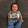 baby, child, smiling, sitting, blue_overalls, elephant_patch, striped_shirt, couch, gray_fabric, barefoot, happy, indoors, portrait, cute, playful, person, infant, face, hand, foot