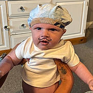 Harrison joined the competition — help win amazing prizes! baby, infant, child, hat, white_shirt, tattoo, hand, face, mustache_drawing, indoor, carpet, cabinet, drawer_knobs, person, cute, adorable, holding, skin, expression, closeup