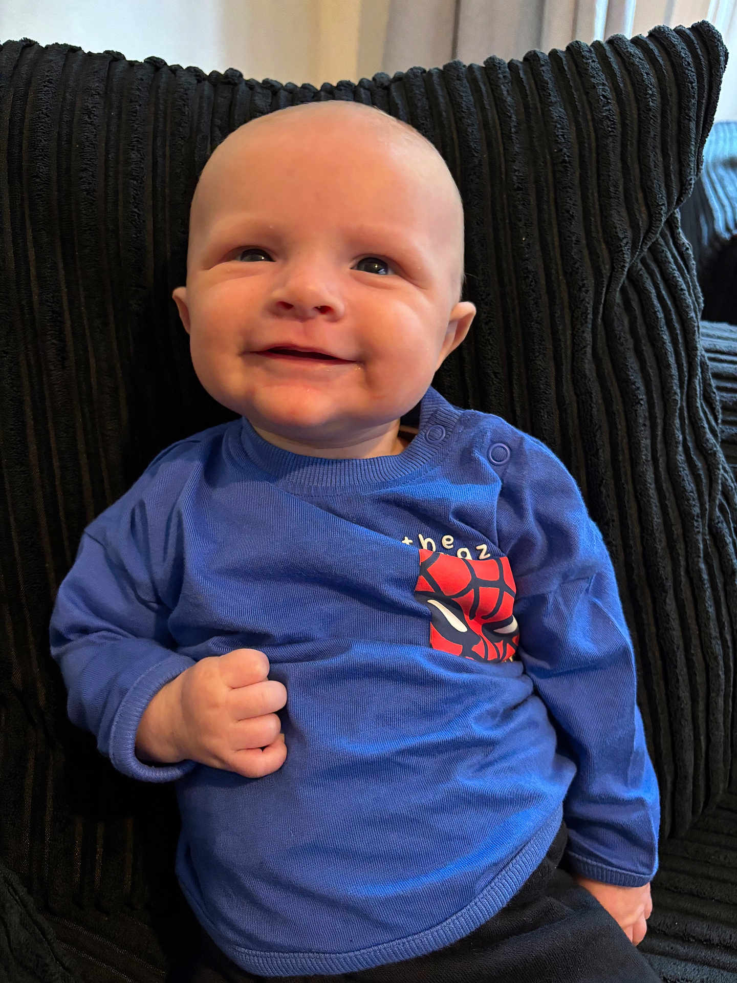 Harrison is registered to the contest to win money with this photo: baby, child, smiling, blue_shirt, couch, cushion, indoor, portrait, happy, infant, person, sitting, fist, clothing, head, face, young_child, cute, comfort, young